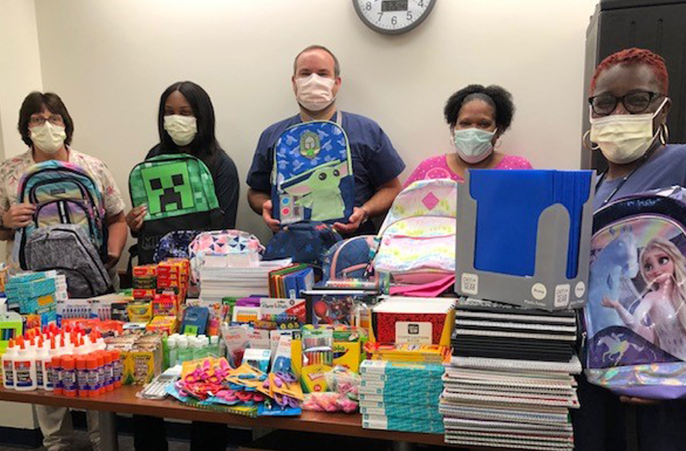 Five masked staff members from the HUP Nursing Network Center hold up colorful and themed backpacks